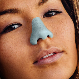 Close up view of a woman’s face wearing blue Nöz Nözscreen on her nose